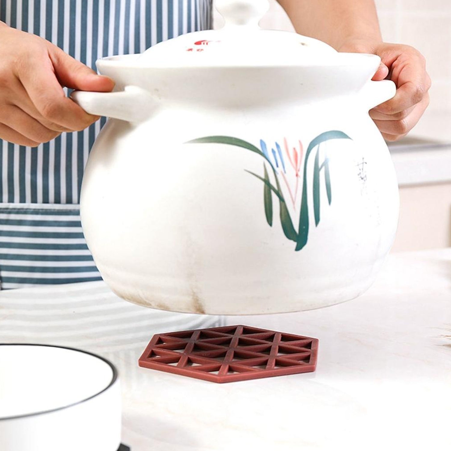 Person placing a large white ceramic pot on a red PVC tea coaster, showcasing its heat-resistant and anti-slip properties.